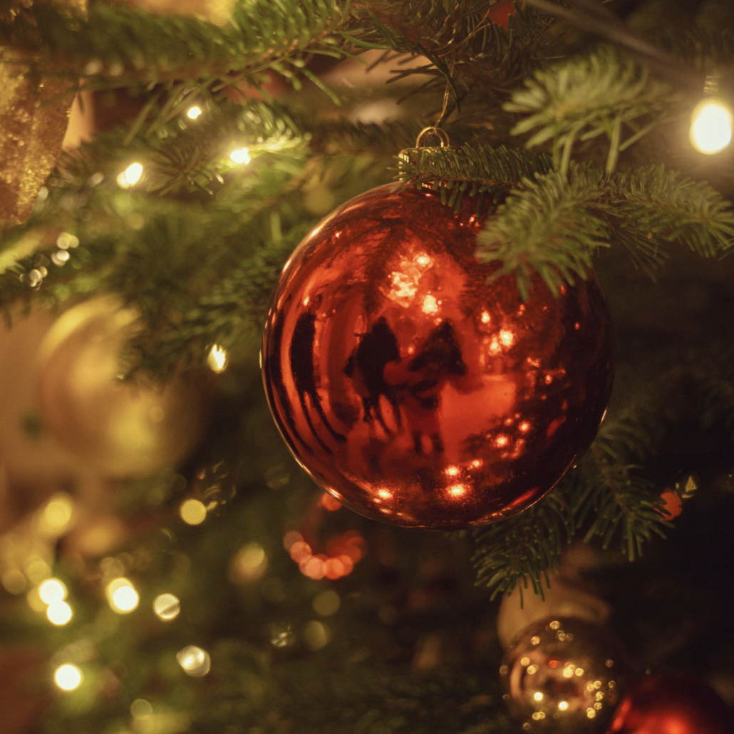 A traditional Christmas decoration Red glass bauble hanging among fir branches and warm Christmas lights