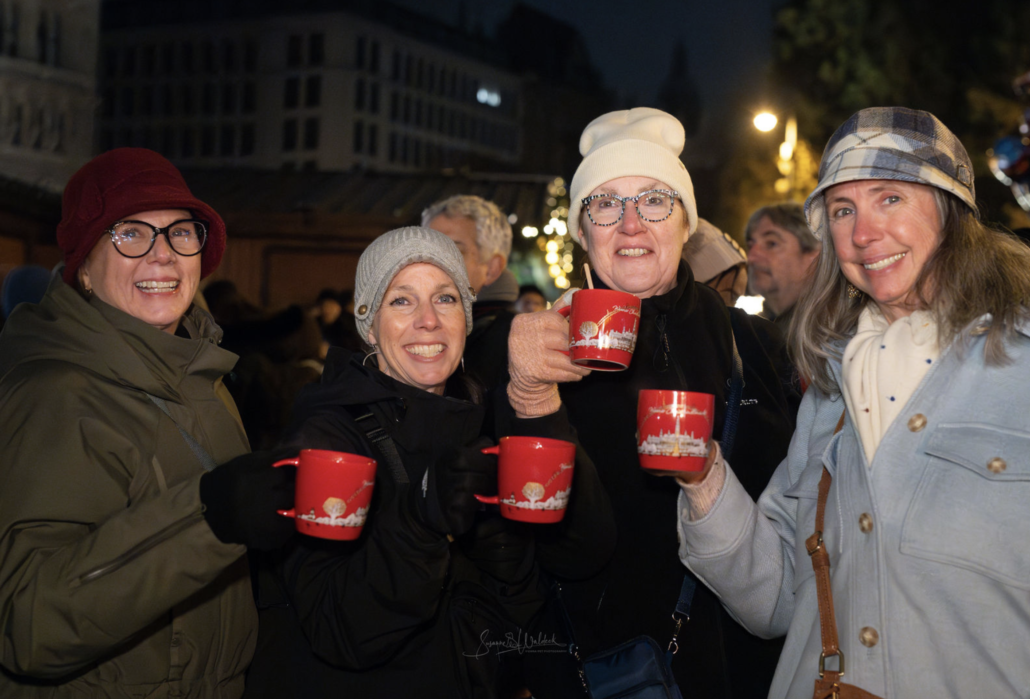 Christmas market tour guests Four smiling guests holding red punch mugs at a Vienna Christmas market