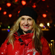 Susanne Waldeck – Vienna Christmas Market Tour Susanne Waldeck in a red jacket with Christmas lights in Vienna