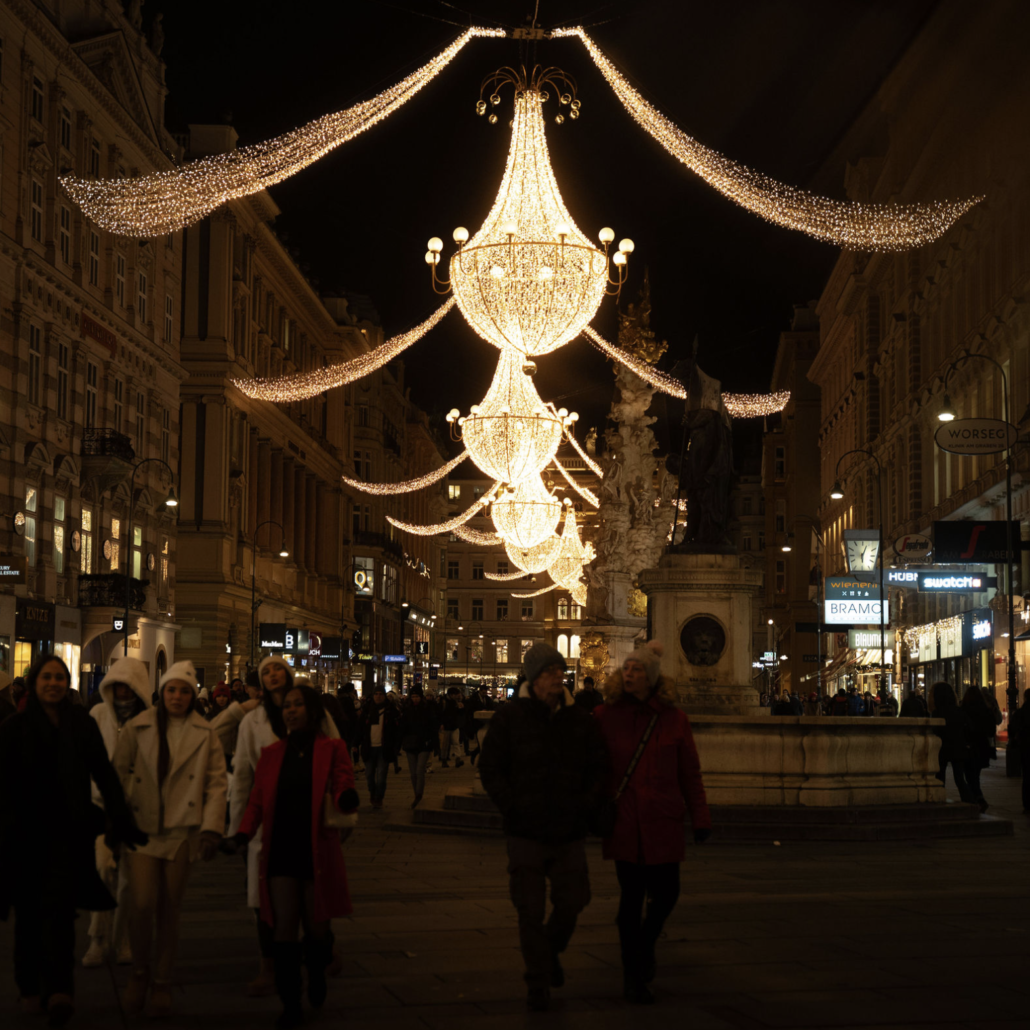 Christmas lights on the Graben People walking beneath golden chandelier Christmas lights on Vienna’s Graben